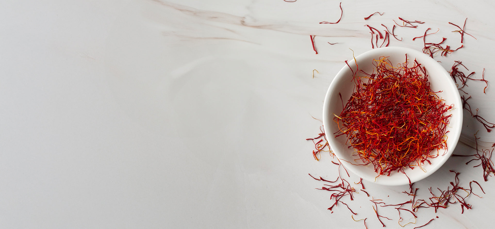 White bowl filled with saffron threads on a light gray background