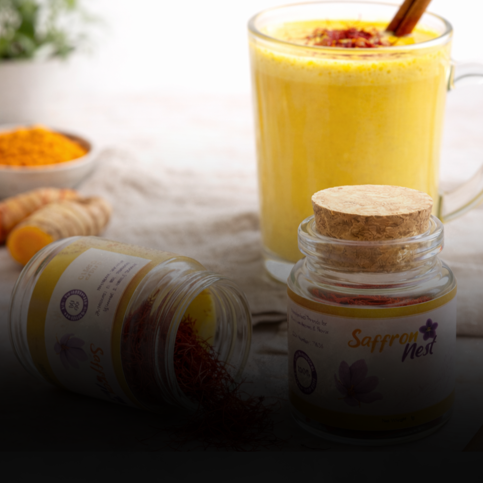 Glass of yellow turmeric latte with spices and 'Saffron Nest' jar on a light background